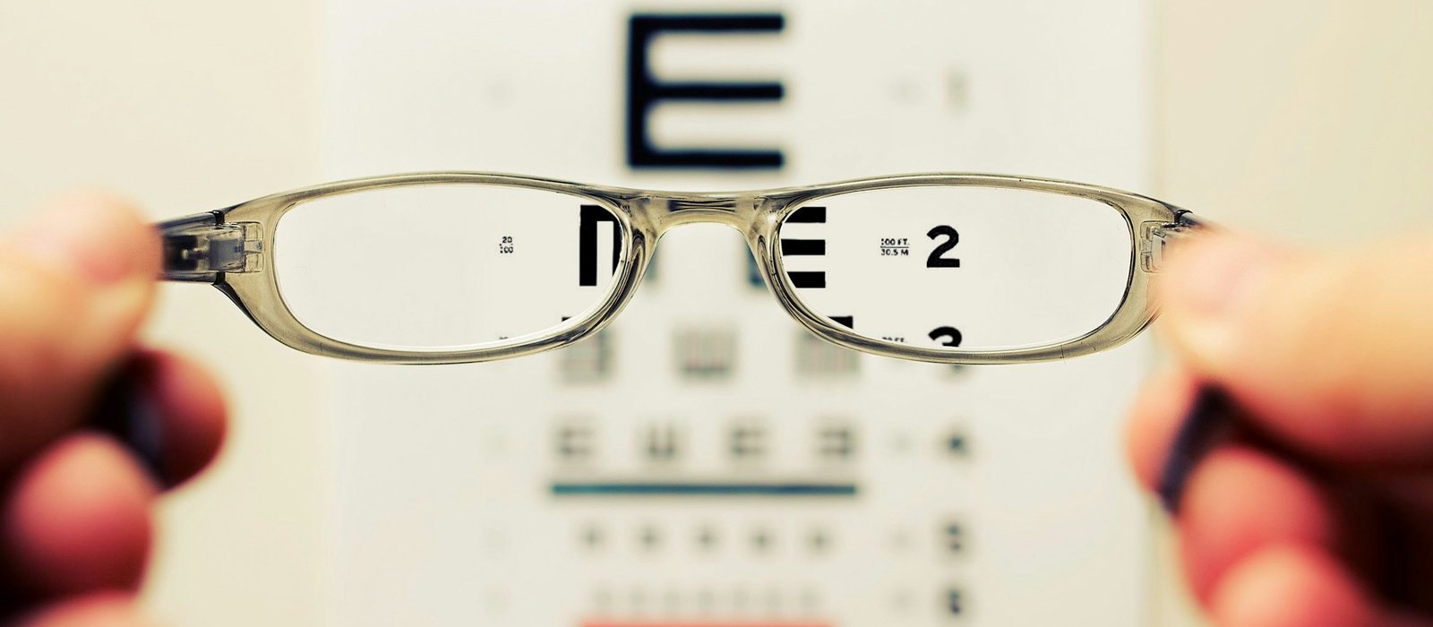 Glasses held up in front of a wall mounted sight test chart